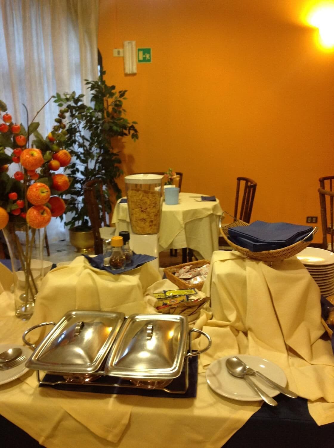 A buffet setup with multiple serving trays, a vase of oranges, and a table with a white tablecloth.