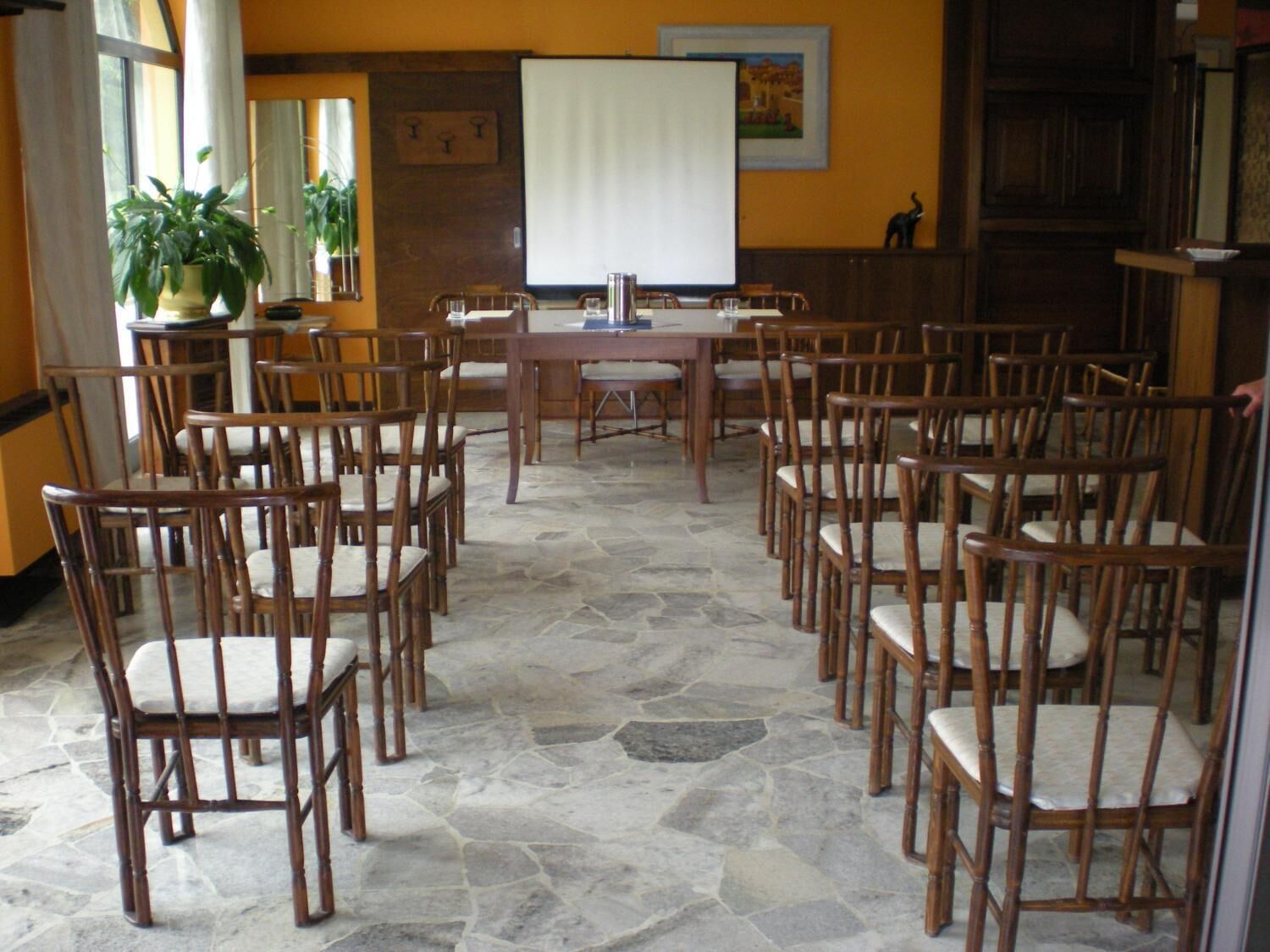 A conference room with a large table and multiple chairs, stone flooring, and a potted plant.