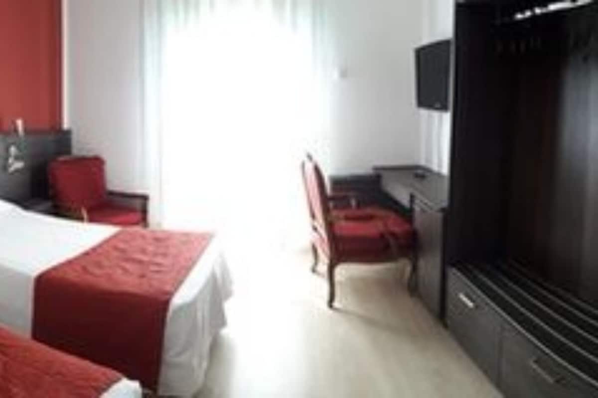 A hotel room with two beds, a TV, and a red wall.