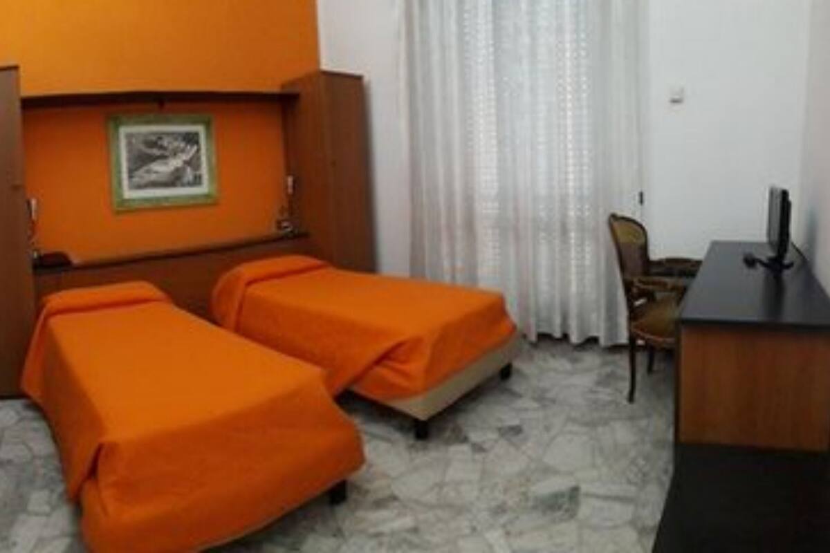 A hotel room with two single beds, a desk, a chair, and a framed picture on the wall.
