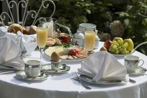 A breakfast table set outdoors with various food items, cups, and a pitcher of juice.