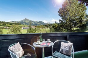 A balcony with a table and chairs, overlooking a mountainous landscape.