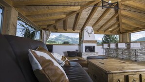 Interior acogedor de una cabaña con techo de madera, chimenea, pared de piedra y vistas a la montaña.