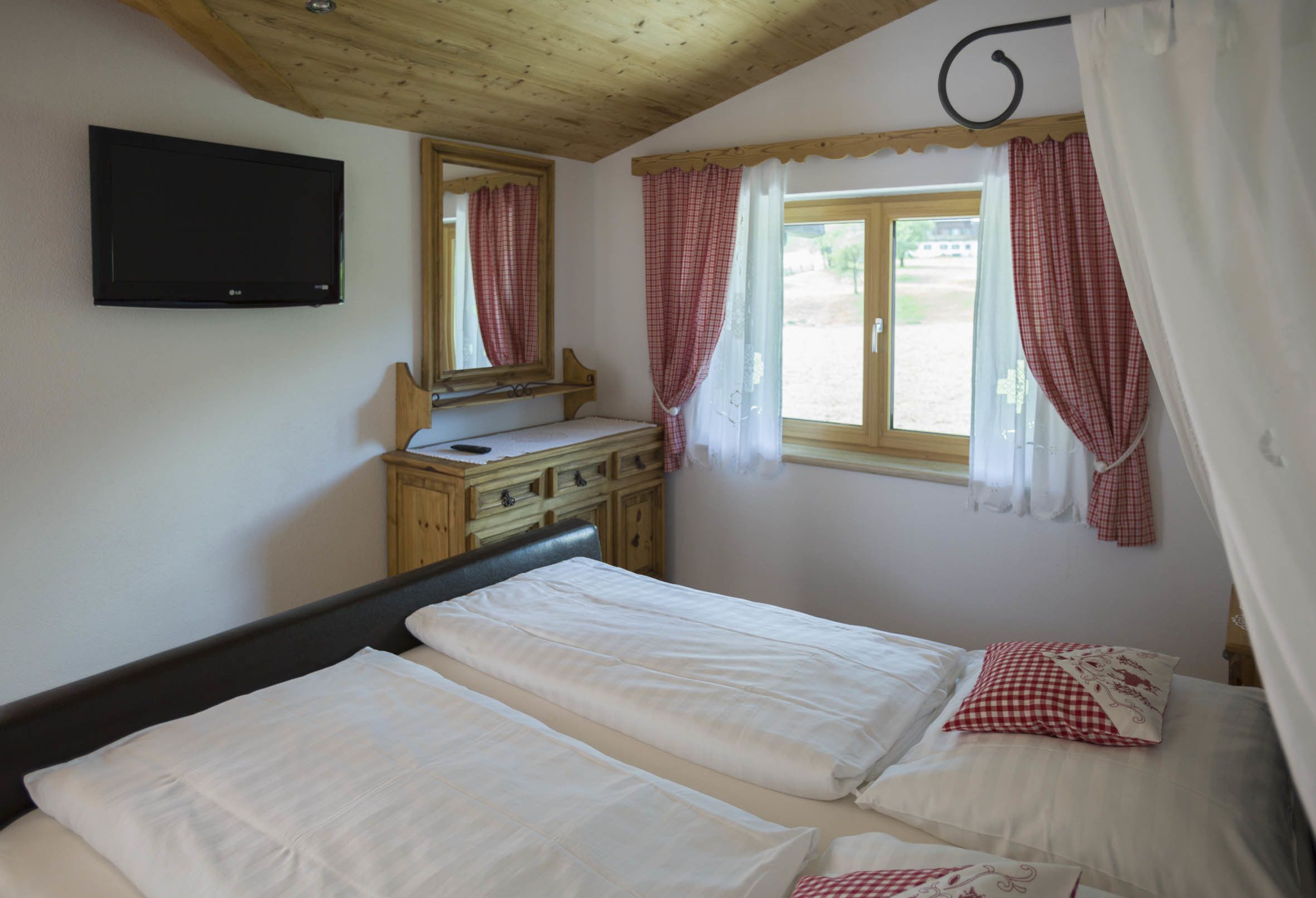 A bedroom with two beds, a wooden dresser, a mirror, and a TV mounted on the wall.