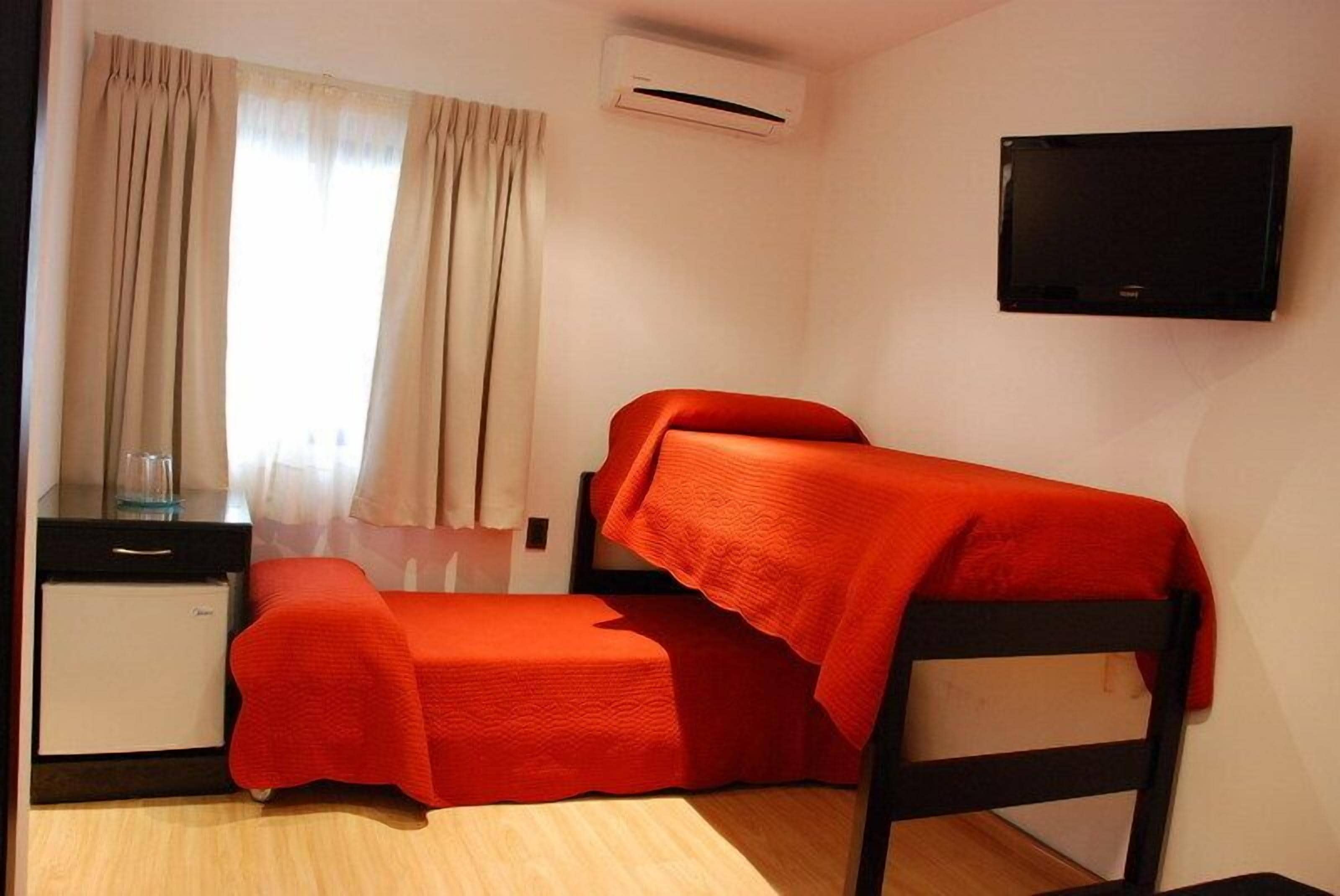 Una camera piccola con un letto a castello, una scrivania con una sedia, una televisione montata a parete e un condizionatore d'aria.