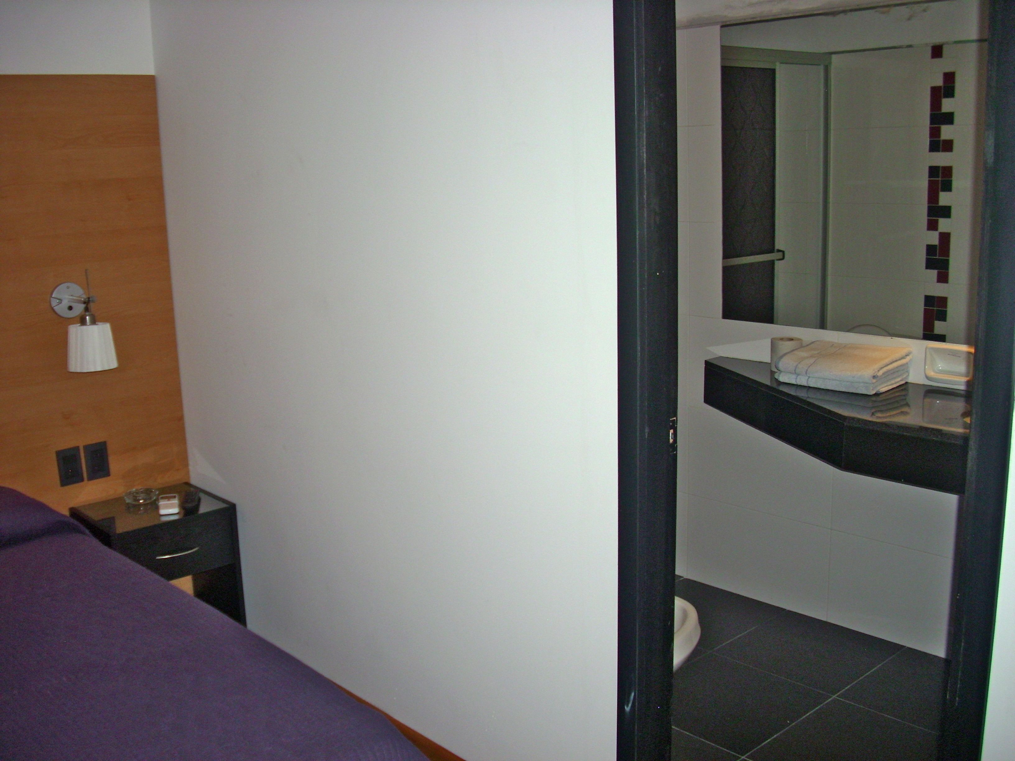 A hotel room with a bed, a nightstand, a mirror, and a bathroom with a toilet and sink.