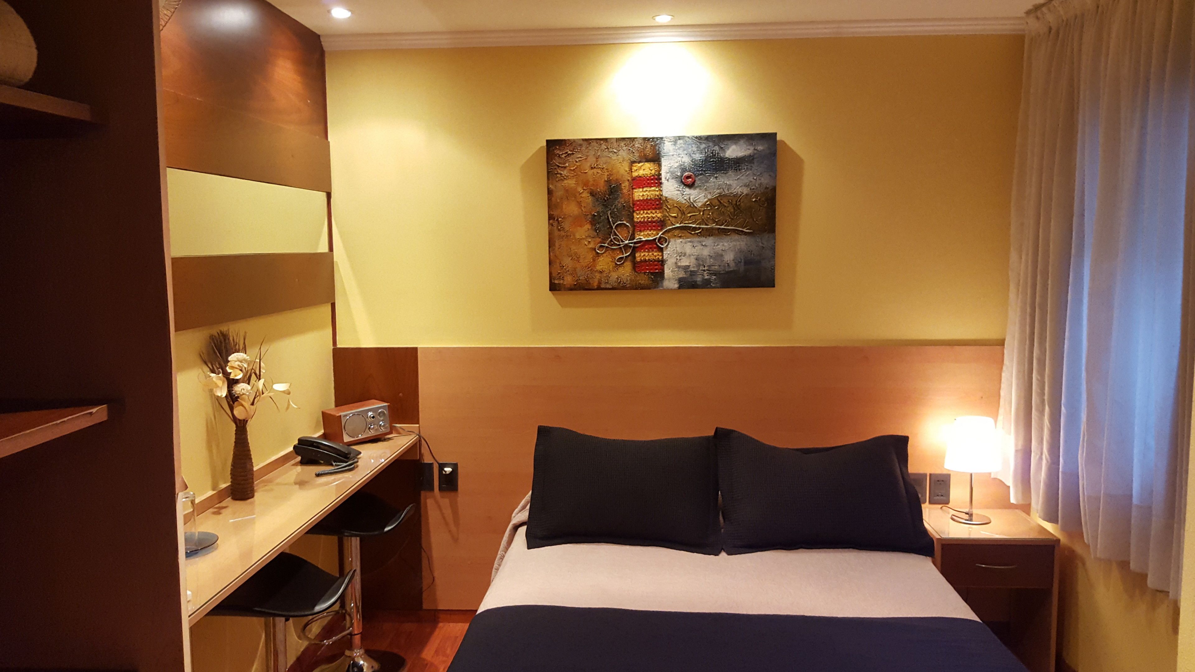 Habitación de hotel con cama, escritorio, silla, lámpara y cuadros en la pared.