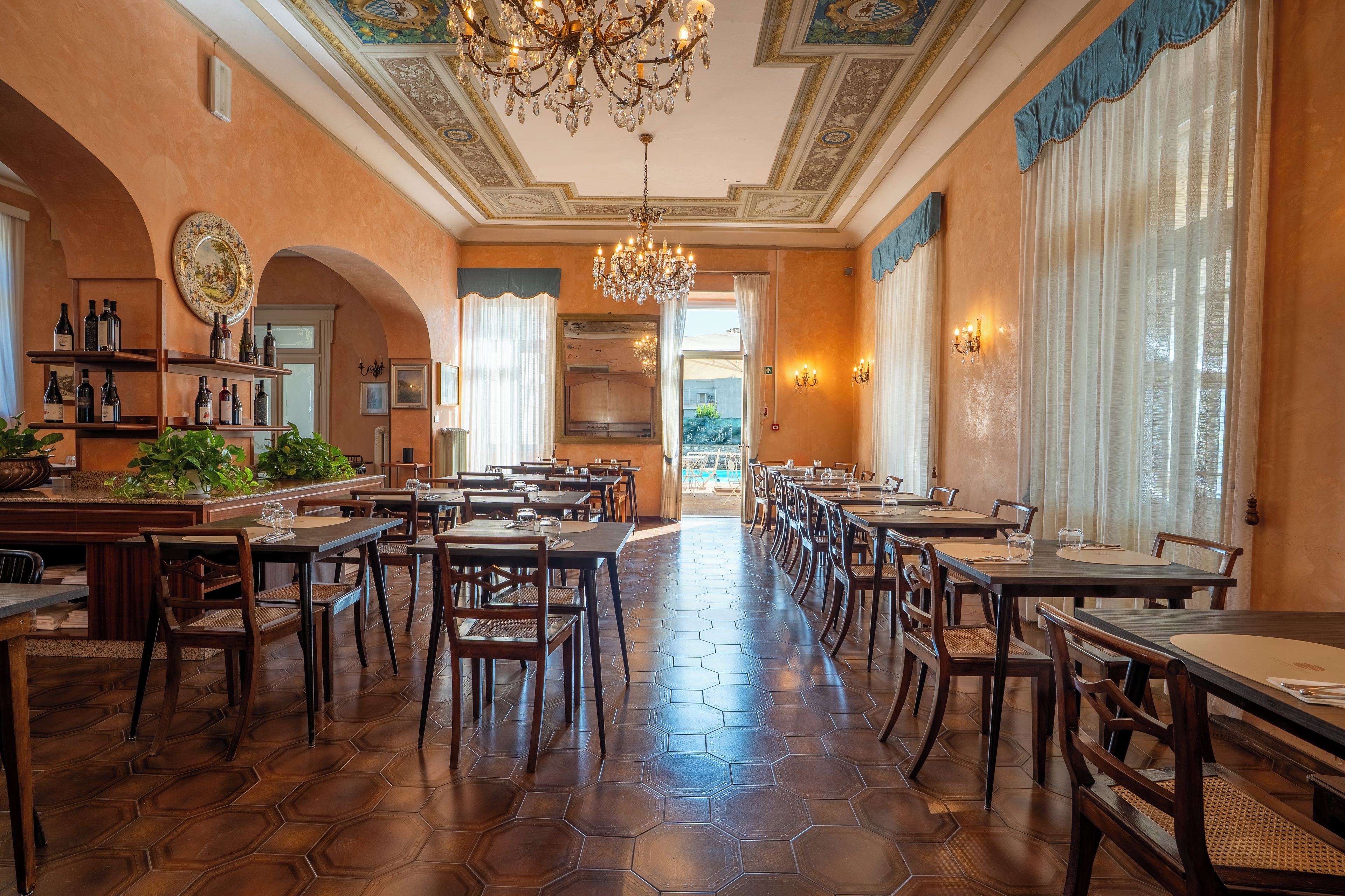 A spacious dining area with hexagonal patterned flooring, wooden tables and chairs, and a chandelier.
