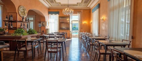 A spacious dining area with hexagonal patterned flooring, wooden tables and chairs, and a chandelier.