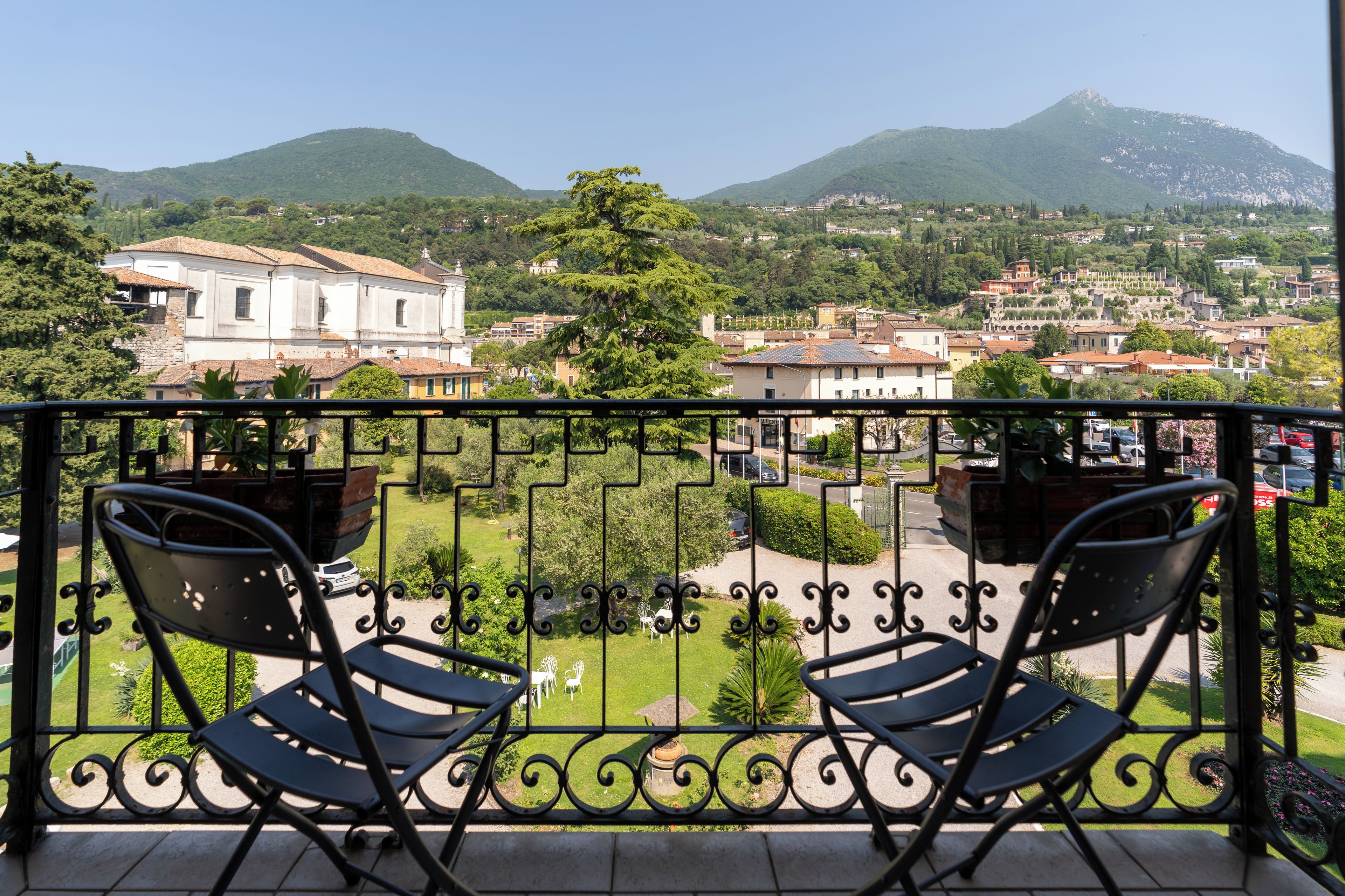 A balcony with two chairs, a view of a town with buildings and mountains in the background.