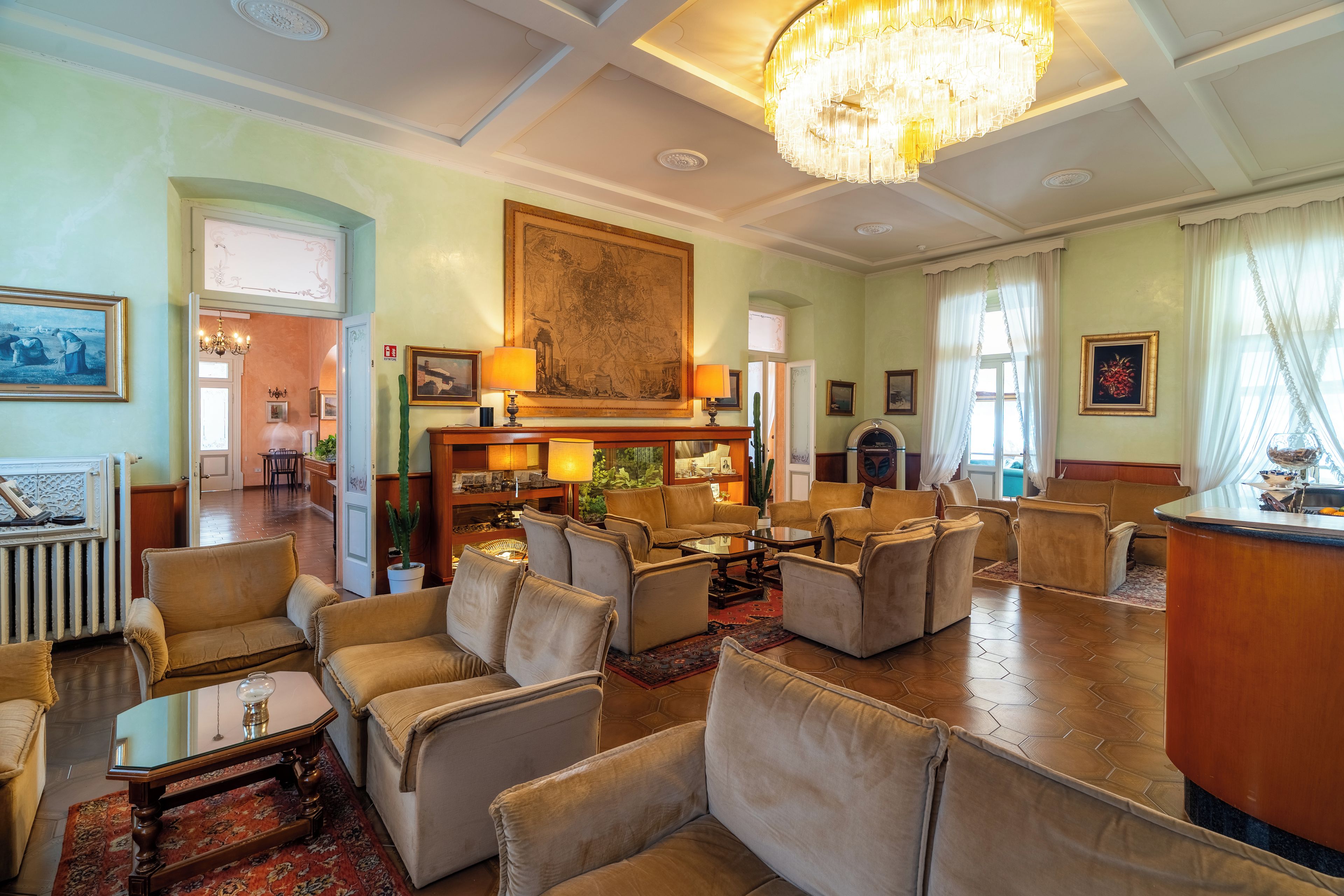 Un'ampia hall d'albergo con diverse zone salotto, un grande lampadario e un quadro di grandi dimensioni appeso alla parete.