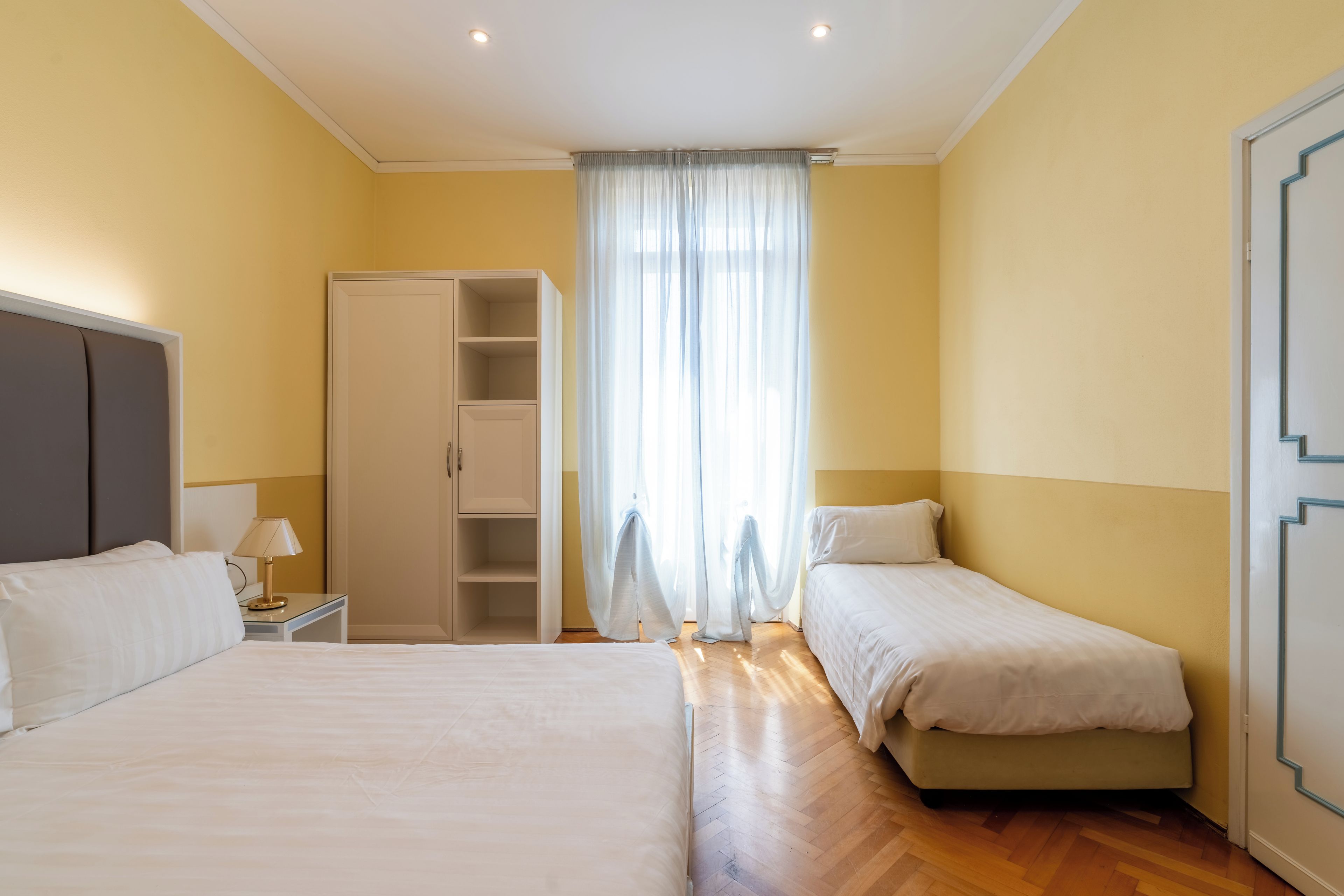 Habitación de hotel con dos camas, un armario, una mesita de noche y una ventana con cortinas.