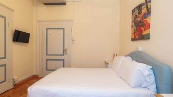 A bedroom with a bed, a flat-screen TV mounted on the wall, a door, and a painting.