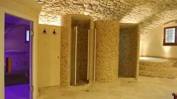 Un baño espacioso con cabina de ducha revestida con mosaicos, una bañera y techo de piedra.