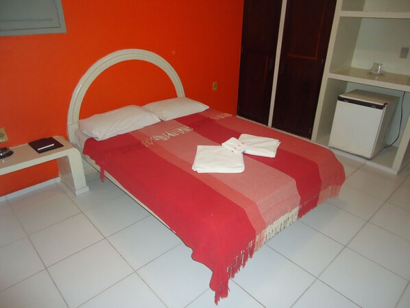 A bed with a red blanket and two towels, a bedside table with a book, and a small white cabinet. - Hotel Pousada Sol (Natal)