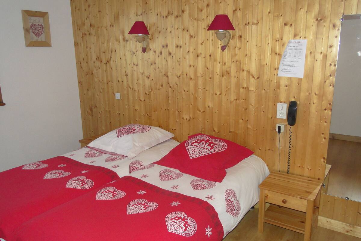 Une pièce aux murs lambrissés, comprenant un lit, deux lampes de chevet, un téléphone sur la table de chevet et une petite table de nuit en bois.
