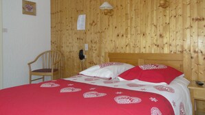 A wooden-paneled room with a bed, a chair, and two wall-mounted lamps. - Le Gotty (La Clusaz)
