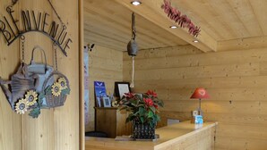 A wooden reception desk with a red rug, a hanging lamp, and a wall-mounted sign. - Le Gotty (La Clusaz)
