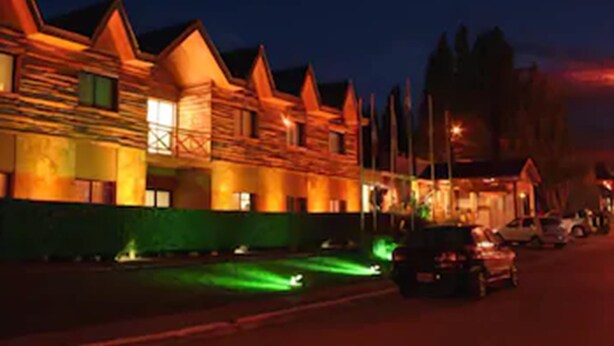Une rangée de bâtiments en bois, dotés de toits à deux versants, qui semblent être un hôtel ou un complexe touristique, de nuit, avec un éclairage public et une voiture garée devant.