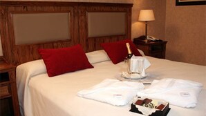 Une chambre d’hôtel avec un lit, des oreillers rouges, une bouteille de champagne et un plateau avec des verres et des serviettes.
