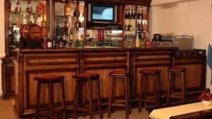 Un coin bar avec des tabourets en bois, un téléviseur fixé au mur et des étagères remplies de bouteilles.