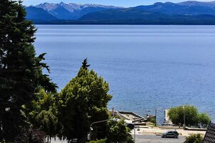 A lake with mountains in the background, surrounded by trees and buildings.