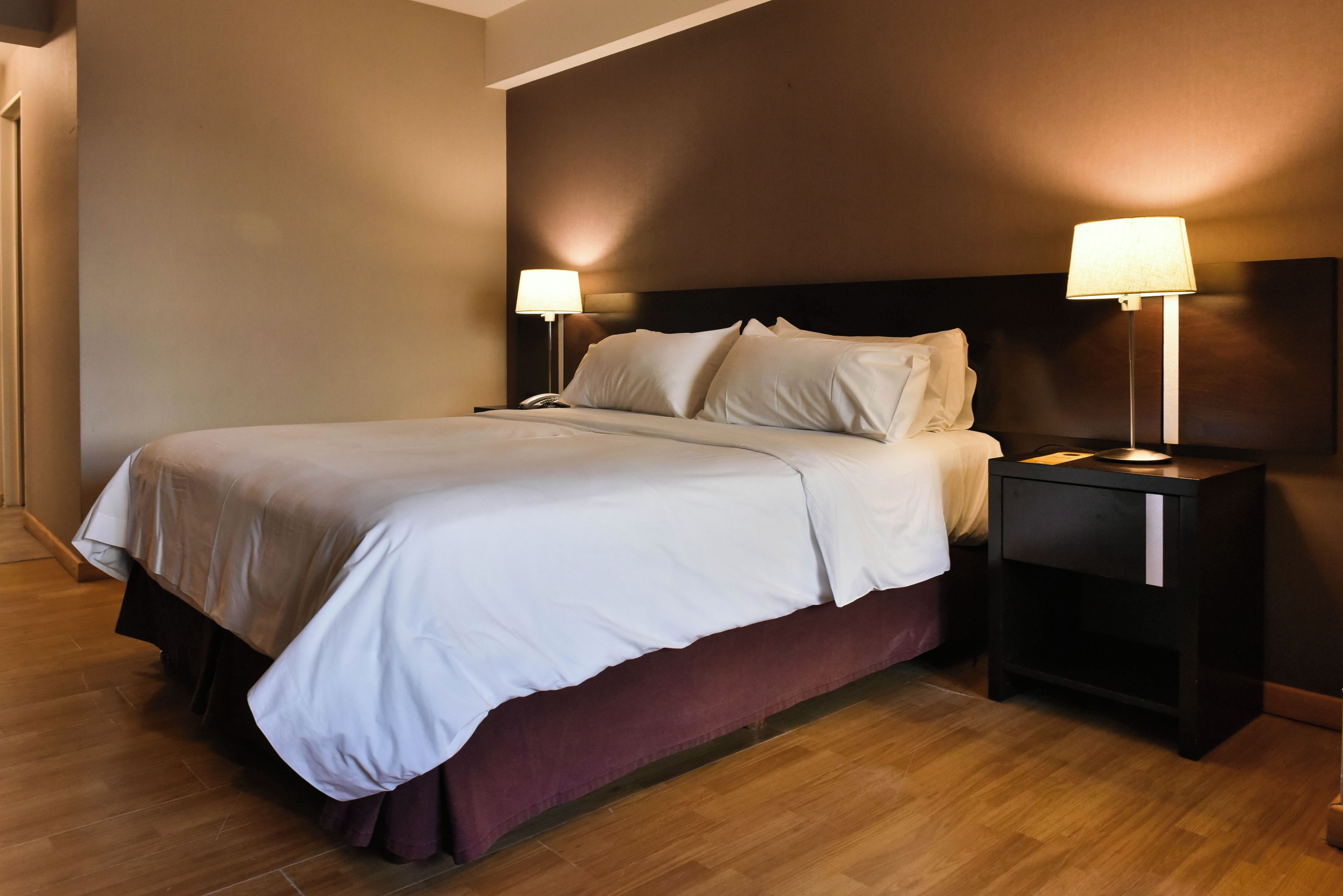 A hotel room with a bed, two bedside tables, and a nightstand.