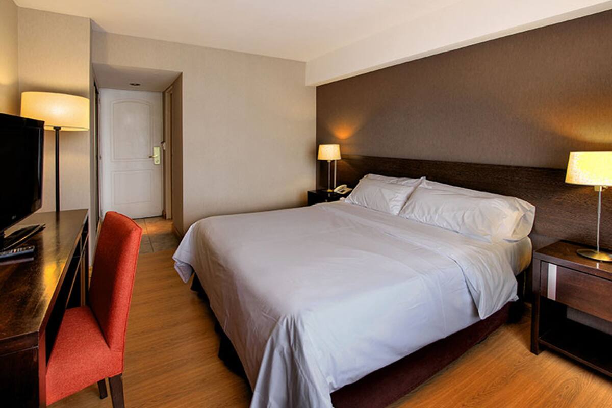 Une chambre d’hôtel avec un grand lit, un bureau avec une chaise, une télévision et deux lampes de chevet.