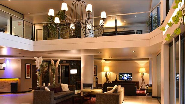 A spacious lobby with a chandelier, sofas, a flat-screen TV, and a balcony with glass railings. - Crans Montana Hotel (San Carlos de Bariloche)