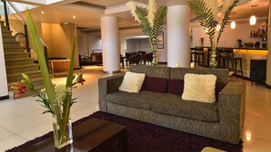 A modern living area with a grey sofa, a coffee table, and a vase with flowers. There is a staircase in the background leading to another level. - Crans Montana Hotel (San Carlos de Bariloche)