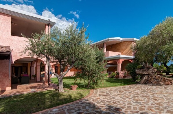 Un edificio con varios balcones, un patio de piedra y abundante vegetación.