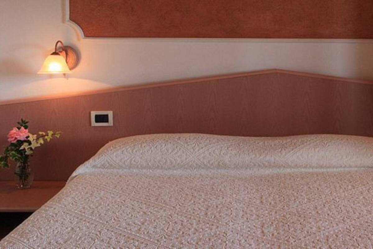 Una cama bien hecha con una colcha estampada, dos mesitas de noche con lámparas y un pequeño jarrón con flores sobre una de ellas.