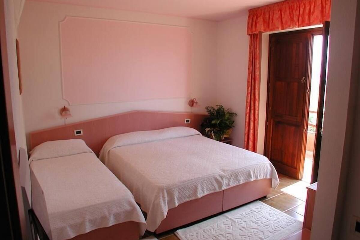 Un dormitorio con dos camas, un ventanal con cortinas y una puerta que da a un espacio exterior.