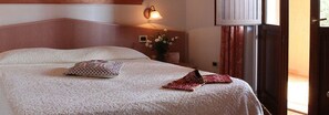 Una cama bien tendida con una almohada estampada y una colcha doblada, una lámpara de pared y un jarrón con flores.