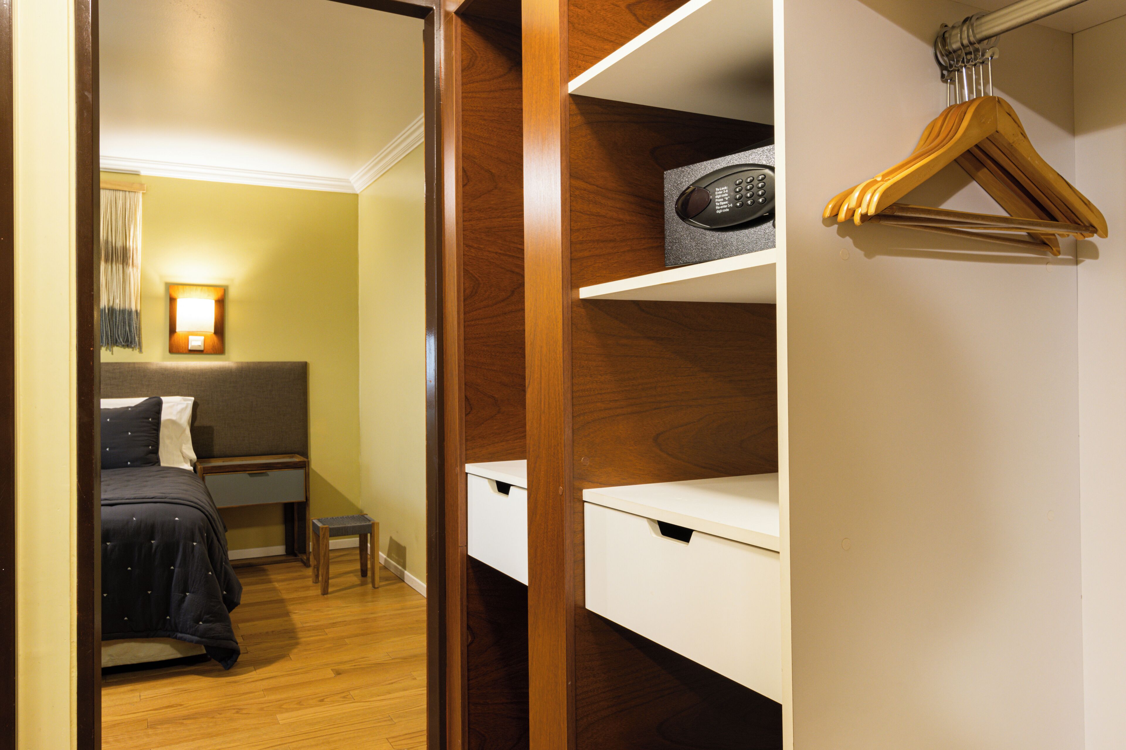 Ein Hotelzimmer mit Bett, Nachttisch und einem Holzschrank mit Regalen und Kleiderhaken.