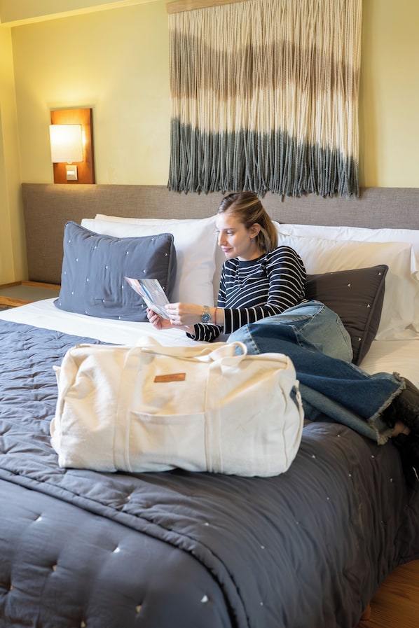 Una persona sentada en una cama con un almohadón, una manta y una bolsa blanca.