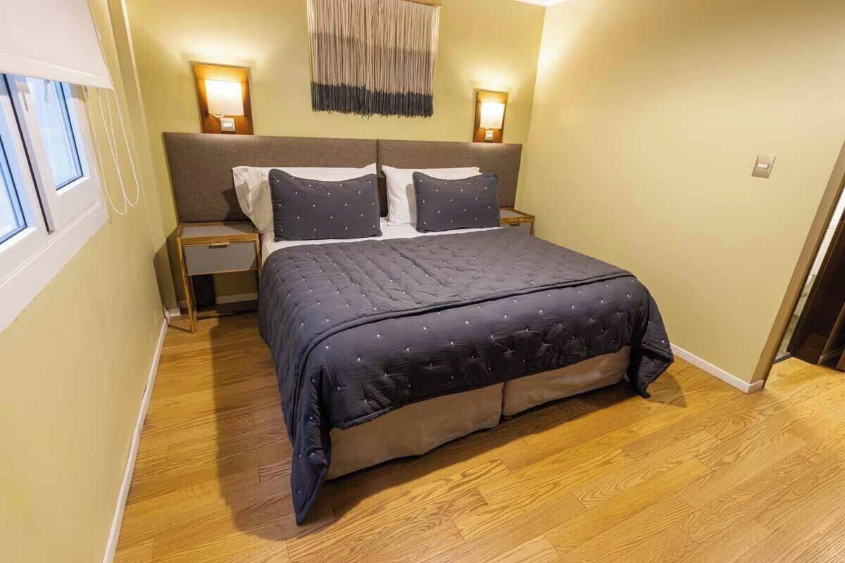 A bedroom with a bed, two bedside tables, a wall-mounted lamp, and a window.