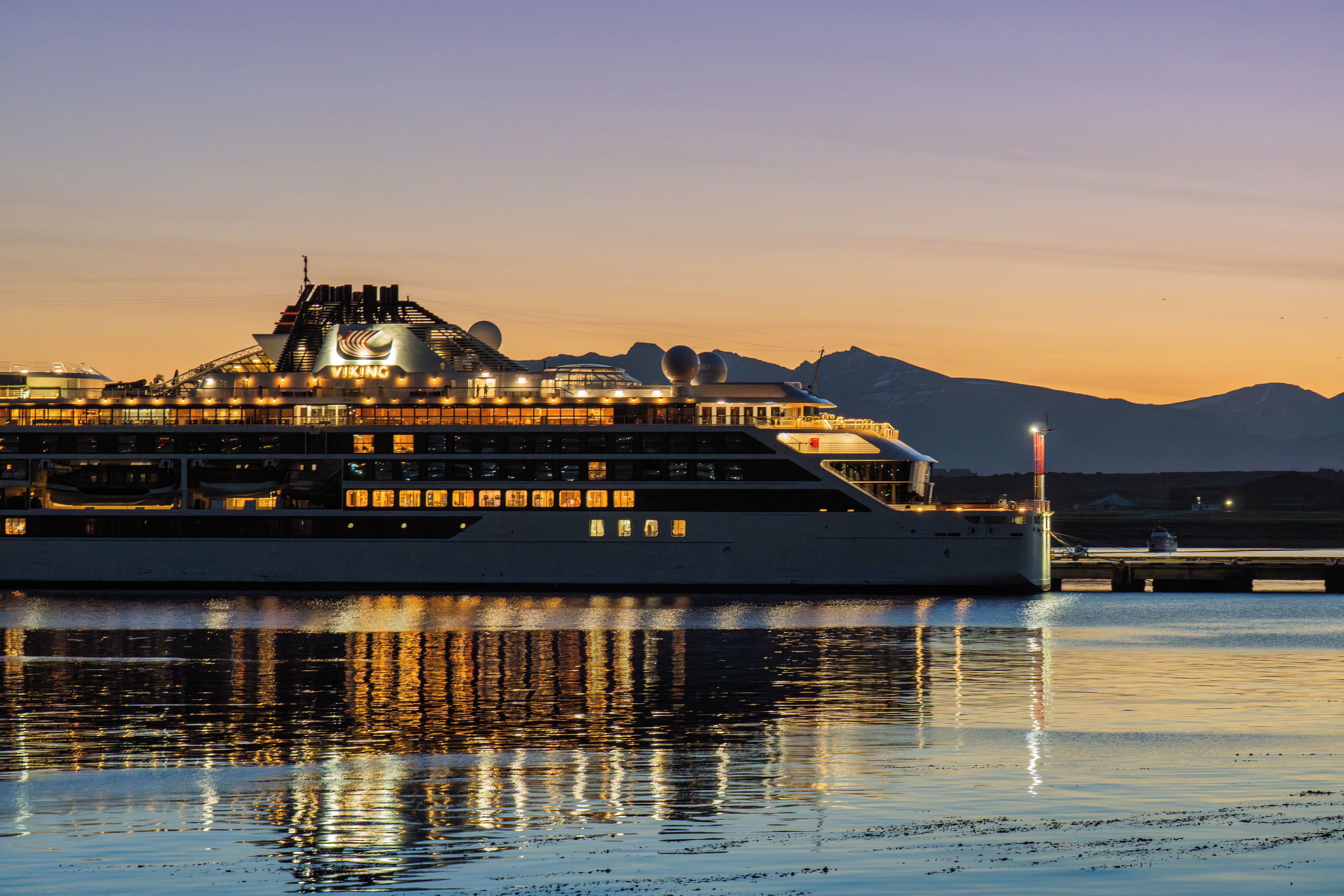 Un grand navire de croisière a accosté dans un port, avec une chaîne de montagnes en toile de fond.
