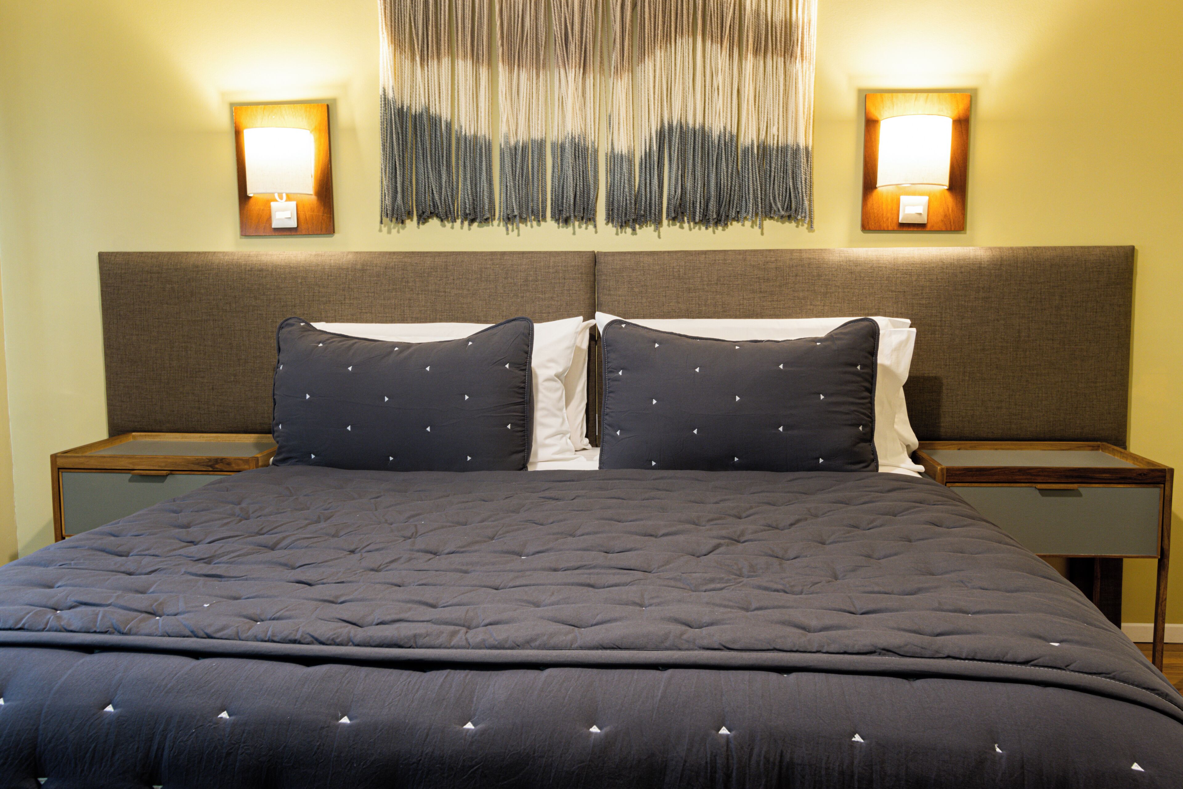 A neatly made bed with a dark quilt and two pillows, flanked by nightstands with lamps.