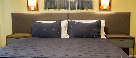 A neatly made bed with a dark quilt and two pillows, flanked by nightstands with lamps.