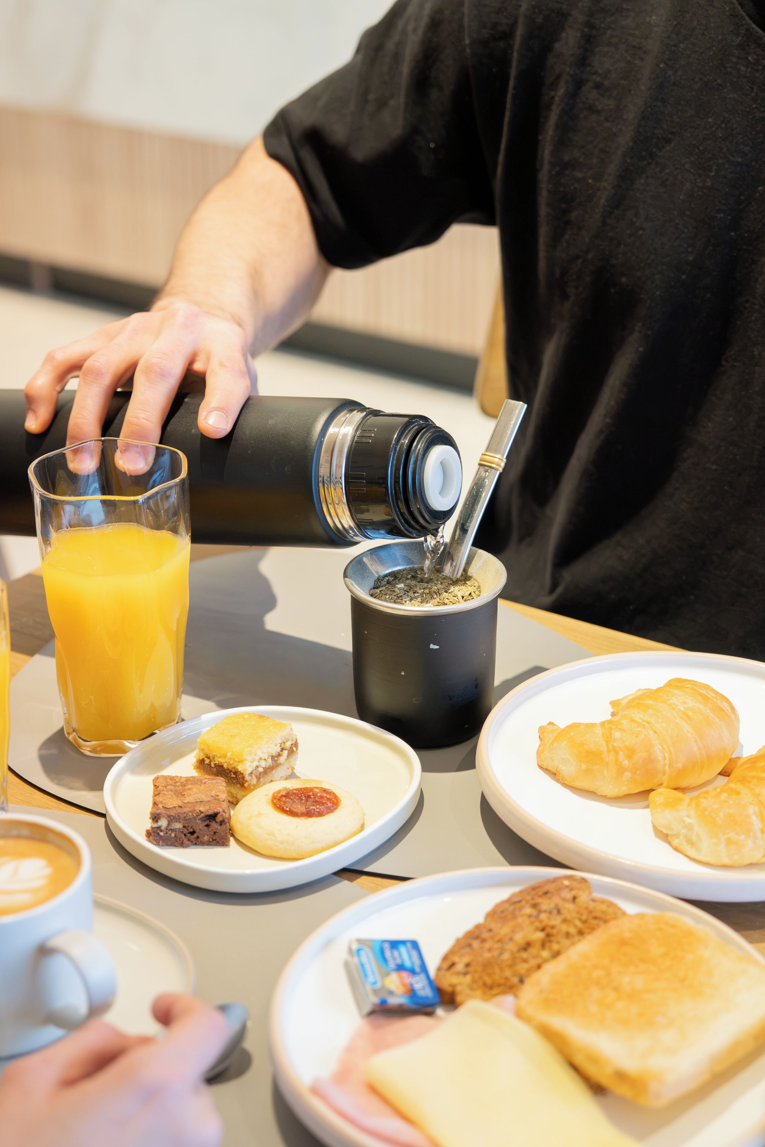 Una colazione con un bicchiere di succo d'arancia, una tazza di caffè e diversi pasticcini su piatti.