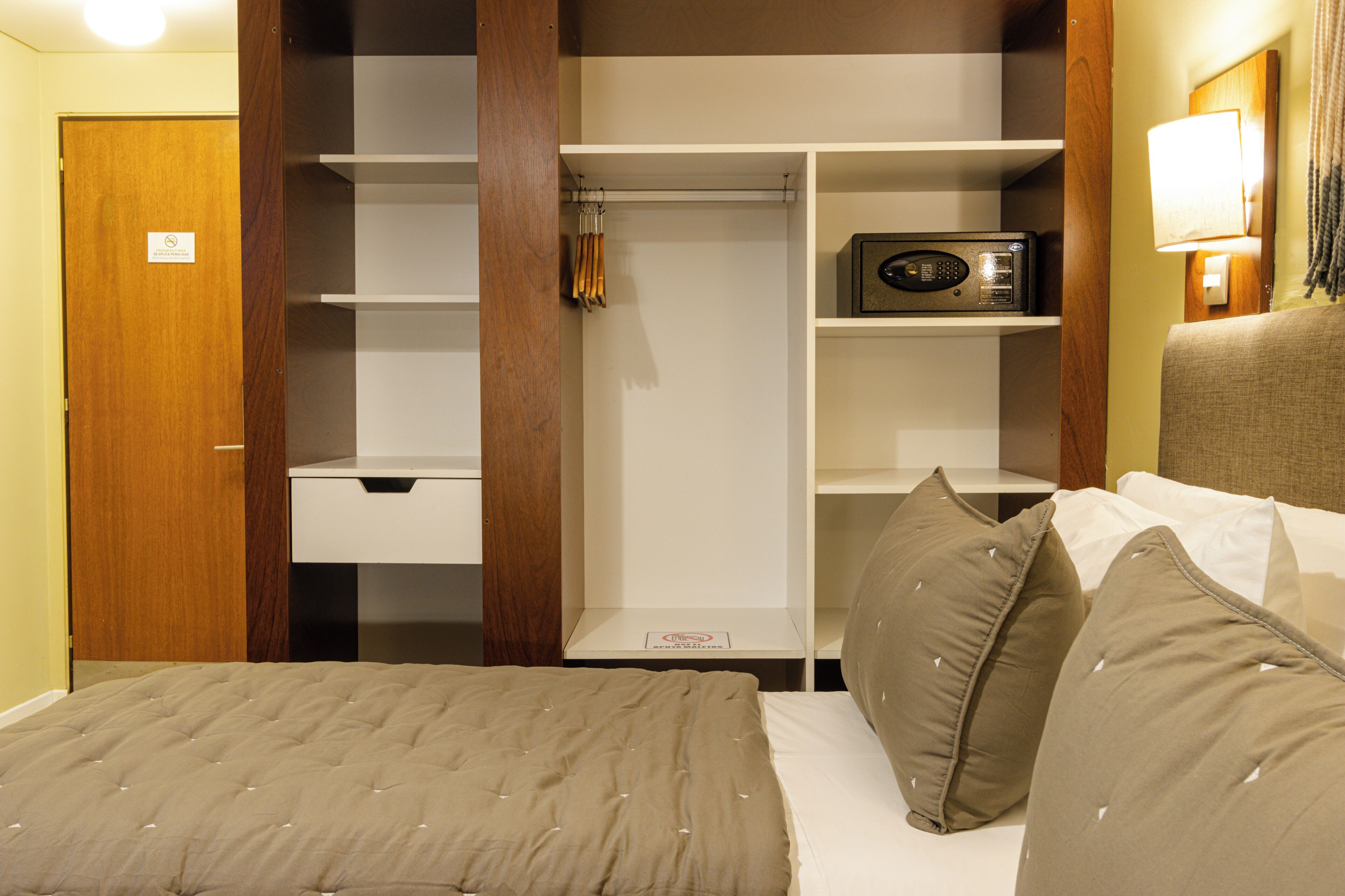 A hotel room with a bed, a wardrobe, and a shelf with a radio.