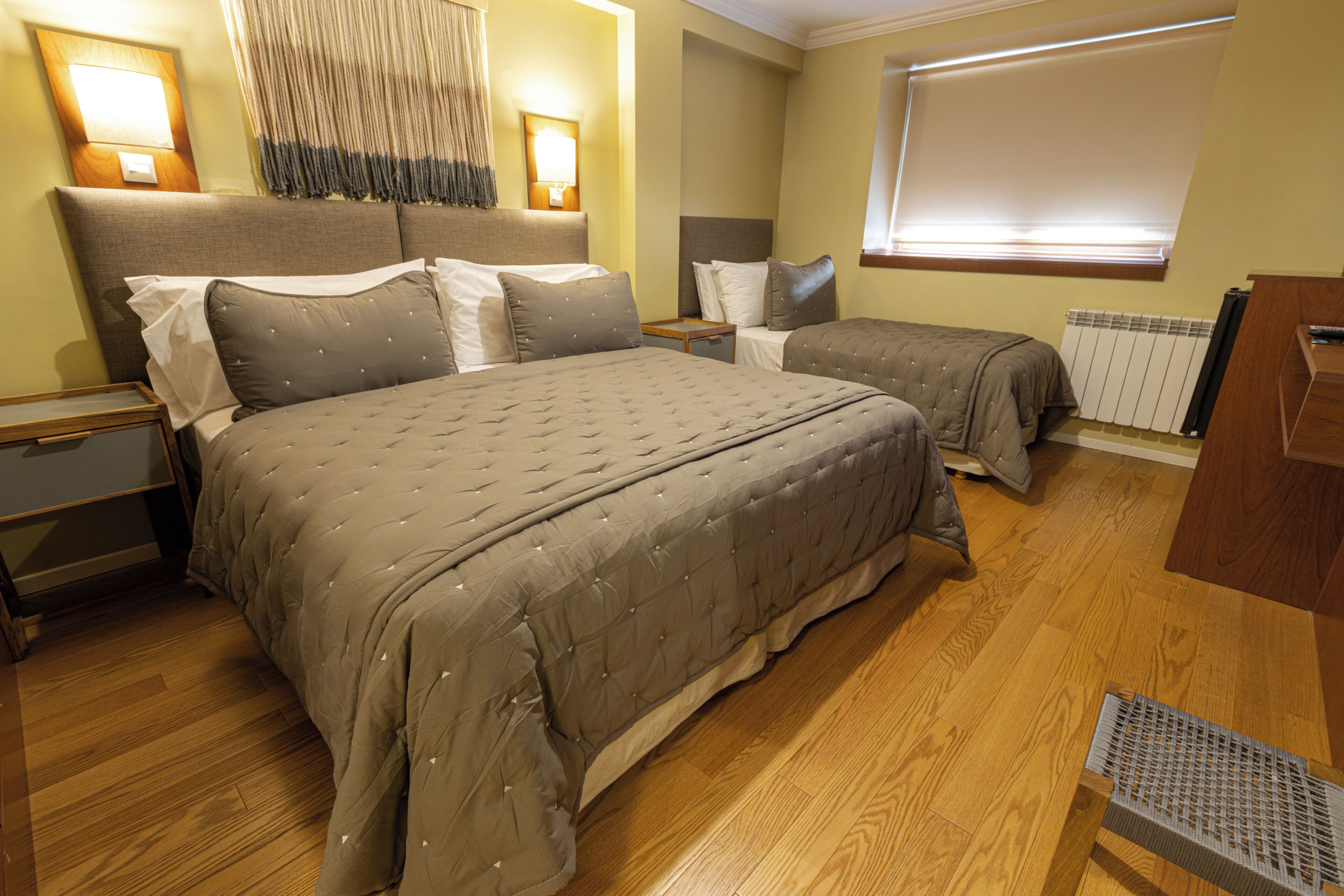A hotel room with a large bed, a smaller bed, wooden flooring, a radiator, and a desk with a chair.