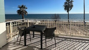 A patio with a table and chairs, overlooking a beach with palm trees and the ocean. - Hotel Ristorante Centosedici (Terracina)