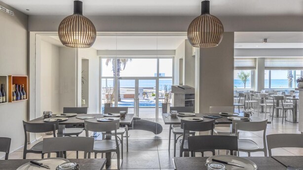 A spacious dining area with tables and chairs, large windows offering a view of the sea, and pendant lighting fixtures. - Hotel Ristorante Centosedici (Terracina)