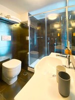 Un baño moderno con ducha envuelta en vidrio, inodoro blanco y un lavamanos grande de color blanco con espejo arriba.