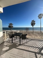 Un patio con mesa y sillas, con vista a una playa con palmeras y el océano.