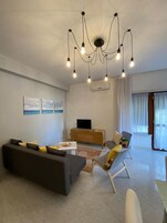 Una sala moderna con sofá, sillón y televisor sobre un mueble de madera.
