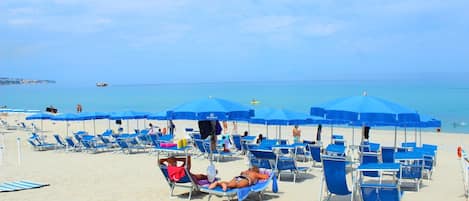 Ein Strand mit Reihen von blauen Liegestühlen und Sonnenschirmen, einem klaren Himmel und ruhiger See.