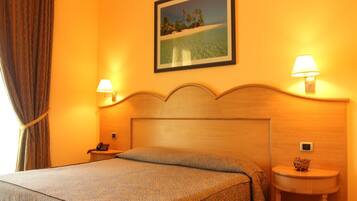Camera d'albergo con un letto, due abat-jour, un comodino, un quadro incorniciato appeso al muro e una finestra con tende.